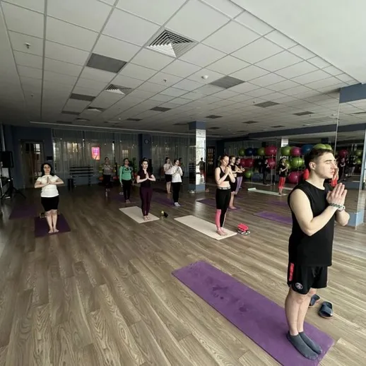 Участники занятий йогой в современном спортивном зале во время вечерней тренировки