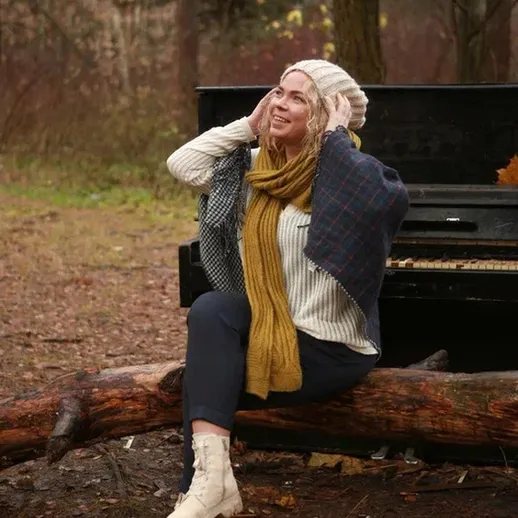 Женщина в уютном шарфе отдыхает на бревне рядом с пианино на фоне осеннего леса