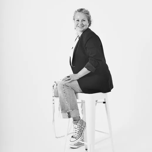 Женщина в стильном пиджаке и кроссовках позирует на табурете в студийной обстановке