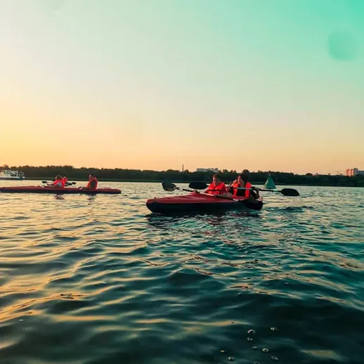 Групповой каякинг на спокойной воде под закатным небом возле города