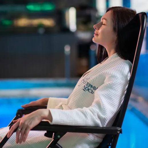 Женщина отдыхает в халате у бассейна в спа-салоне в вечернее время