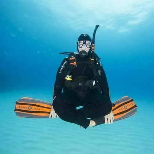 Дайвер в черном снаряжении сидит на подводной доске на фоне бирюзовой воды в тропиках