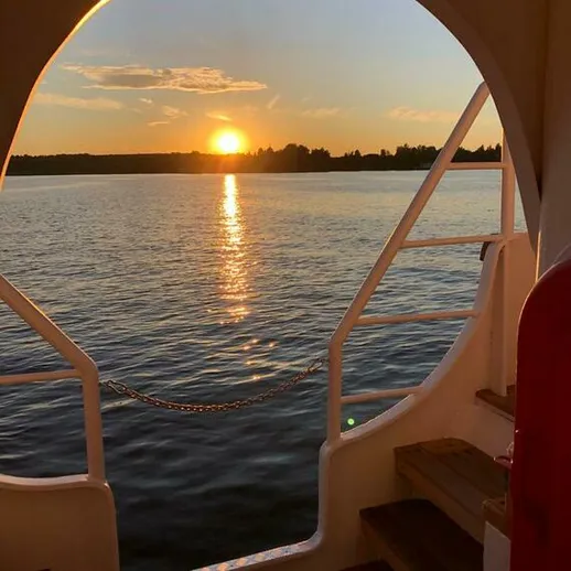 Закат на реке с борта лодки, освещающий спокойную воду и окружающий пейзаж, летний вечер