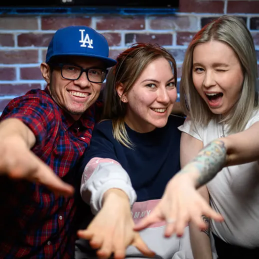 Трое друзей позируют на фоне кирпичной стены в неформальной обстановке с улыбками и позитивными эмоциями