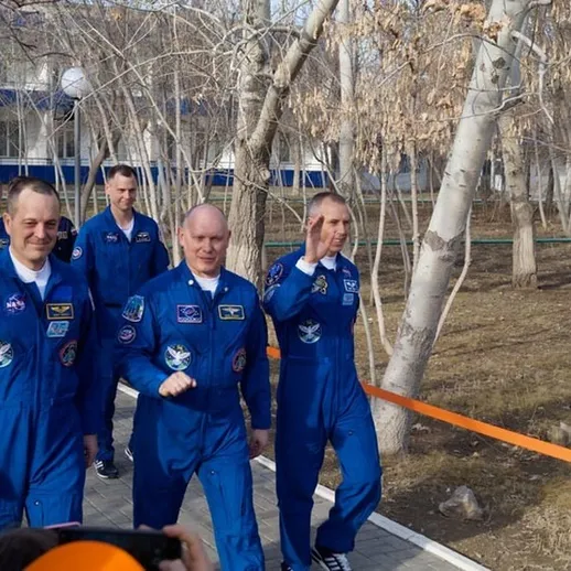 Группа космонавтов в синем скафандре прогуливается по территории космодрома в ясный день