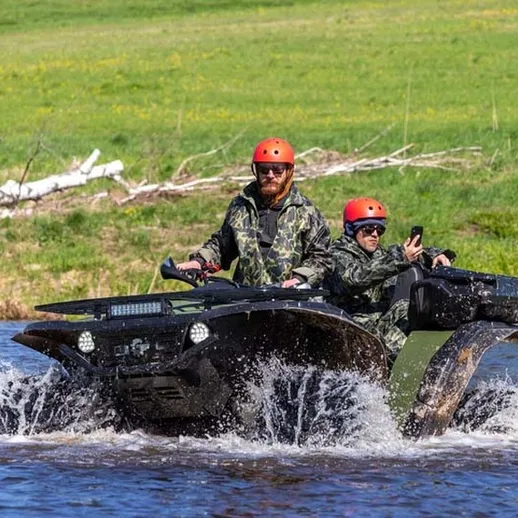 Два человека на вездеходе пересекают реку в живописной местности весной