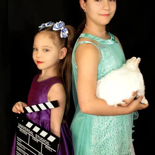 Две девочки позируют на черном фоне, одна держит кролика, другая с клепкой в руках