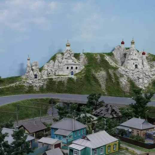 Церковь на холме над небольшим поселком с зелеными домами и дорогой, в ясный день с голубым небом