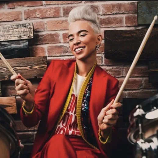 Молодая женщина играет на барабанах, сидя на стуле в студии с кирпичными стенами и деревянными панелями