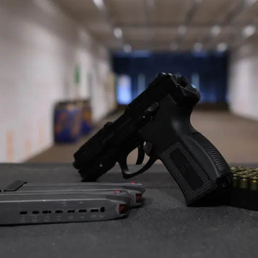 Пистолет и магазин с патронами на столе в тире, готовые к стрельбе в вечернее время