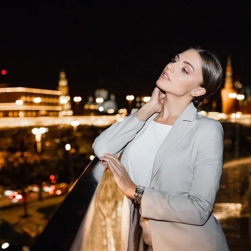 Молодая женщина в светлом костюме позирует на фоне ночной Москвы с яркими огнями