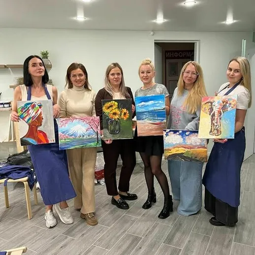 Женщины с картинами на мастер-классе по живописи в уютном студийном пространстве