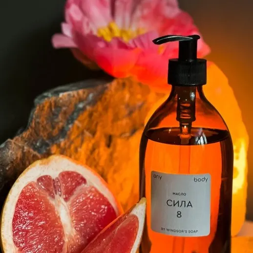 Масло для тела СИЛА 8 на фоне грейпфрута и цветка у камня при мягком свете