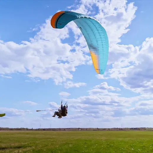 Параплан на фоне голубого неба и облаков над зеленым полем в солнечный день