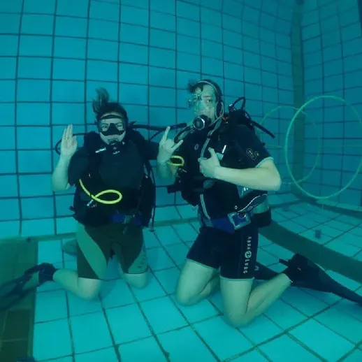 Два дайвера наслаждаются погружением в бассейн в солнечный день, демонстрируя знакомые жесты под водой