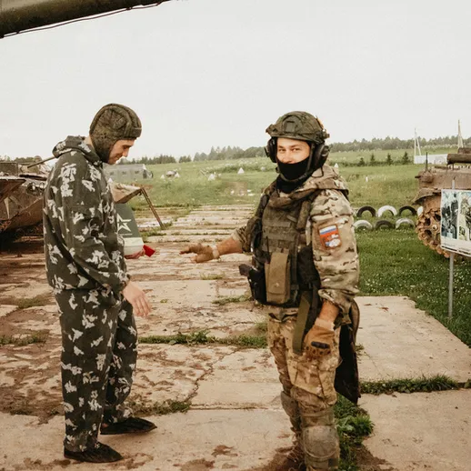 На военной базе два человека обсуждают детали военной техники на фоне танков