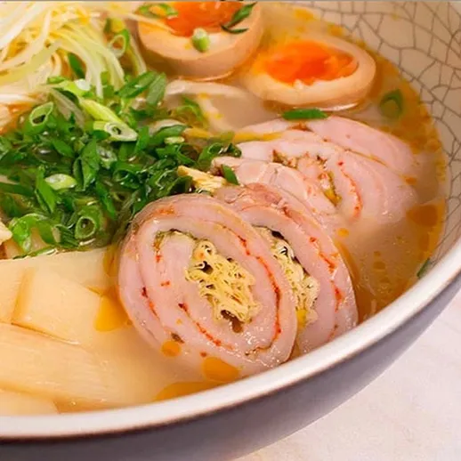 Сытный суп с лапшой, яйцом и мясом нарезкой, поданный в глубокой тарелке, украшен зеленью в японском ресторане