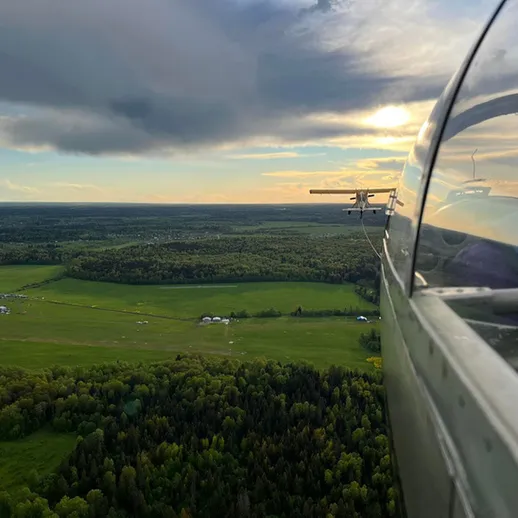 Полет на легком самолете над зелеными полями и лесами в вечернее время близ живописного уголка природы