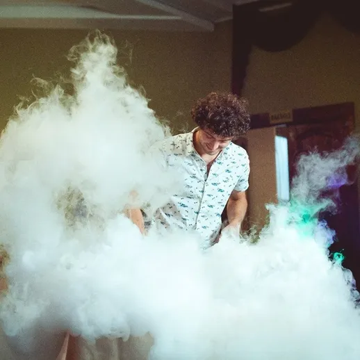 Молодой человек создает облака дыма на вечеринке в уютном помещении с веселой атмосферой