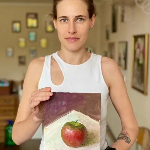 Женщина показывает свою картину с изображением яблока в уютной комнате