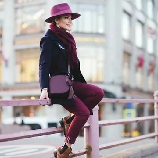 Молодая женщина в стильной шляпе и французском шарфе сидит на ограждении в городском центре осенью