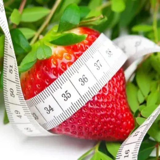 Яркая клубника окружена зеленым растением и измерительной лентой на белом фоне, символизируя здоровое питание