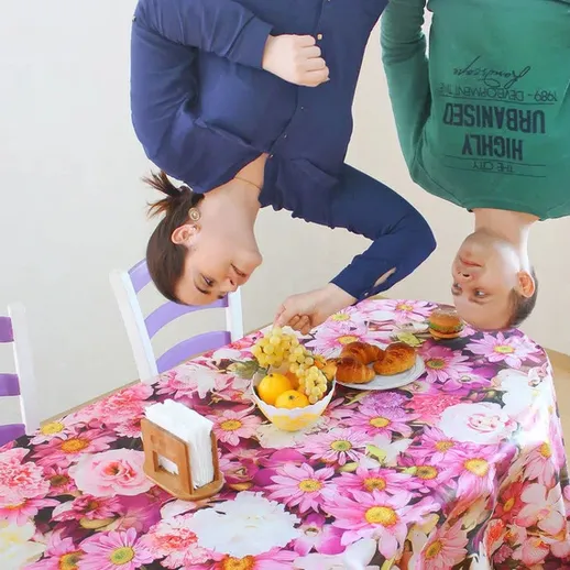 Два человека сидят за столом, перевернутые головы создают забавную иллюзию в светлом помещении