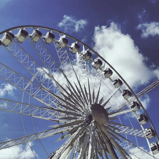 Колесо обозрения на ярком небе с белыми облаками в парке аттракционов