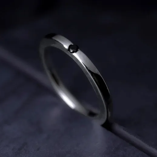 Элегантное кольцо с черным камнем на темном фоне, выделяющееся своей простой, но изысканной формой и текстурой