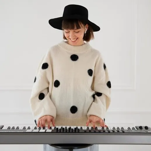 Музыкант исполняет мелодию на клавишах в стильном свитере на фоне белой стены