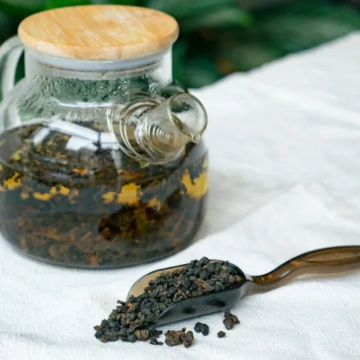 Чайник с заваренным чаем и ложка с улуном на белой ткани