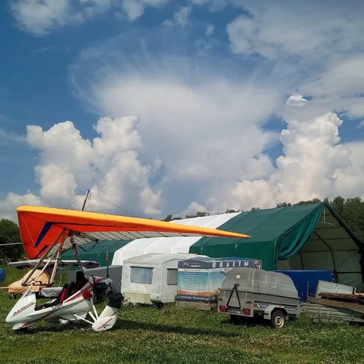 Летательный аппарат рядом с ангаром на фоне облачного неба