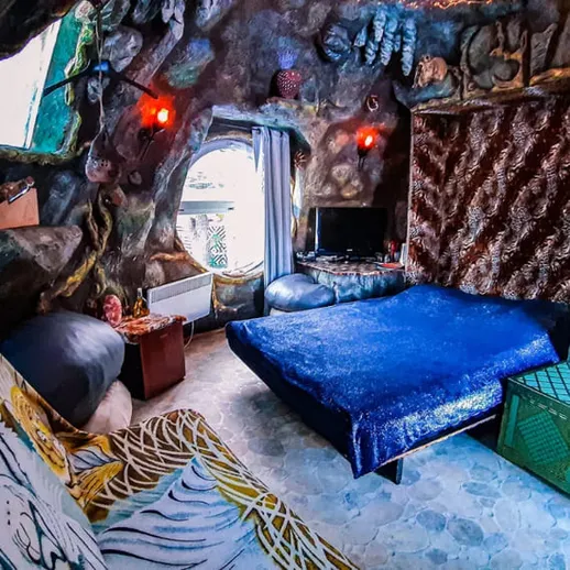 Уютная комната с необычным дизайном внутри каменной структуры на фоне зелени