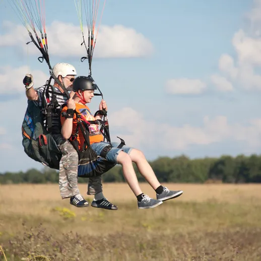 Парапланеристы в воздухе над зеленым полем в ясный солнечный день