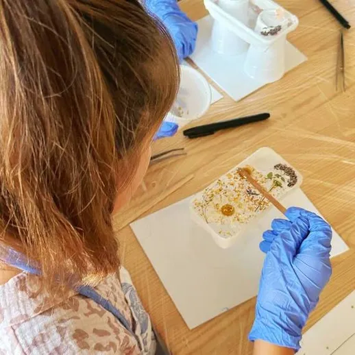 Девушка занимается художественным творчеством в мастерской, создавая уникальные изделия из смолы на деревянном столе