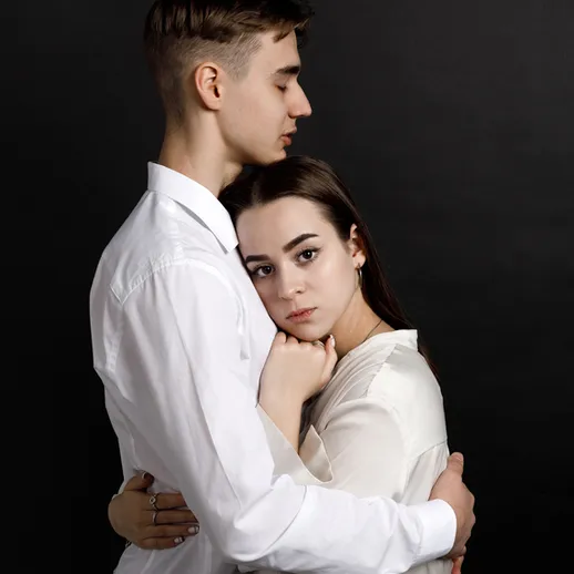 Молодая пара в белых рубашках, обнимающаяся на черном фоне, выражающая нежность и доверие