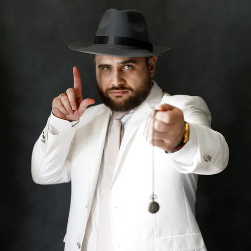 Мужчина в белом костюме с шляпой показывает жест в стильной фотостудии