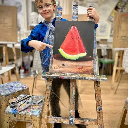 Мальчик показывает свою картину арбуза в классе художественной школы во время занятия по живописи