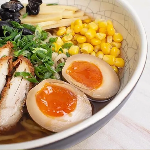 Рамен с курицей, яйцом и кукурузой на столе с зеленым луком и водорослями в уютной обстановке