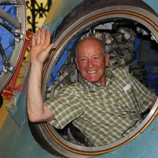 Улыбающийся мужчина машет рукой из окна космического корабля в образовательном центре