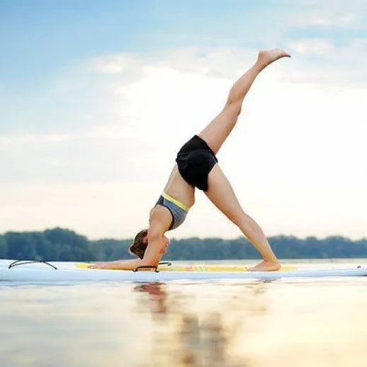 Женщина делает стойку на руках на доске для серфинга на воде в летний день