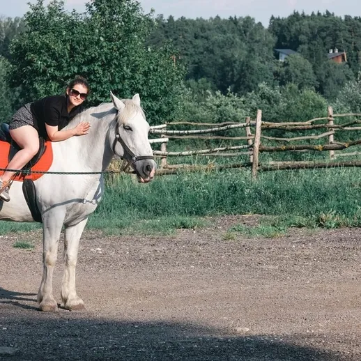 Женщина обнимает белую лошадь на свежем воздухе в зеленом окружении