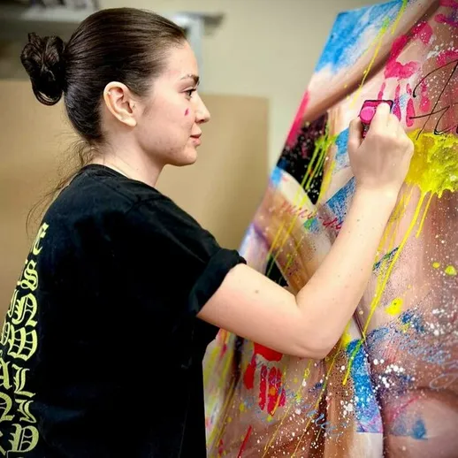 Молодая женщина создает яркий уличный арт в студии, используя аэрозольные краски в процессе работы