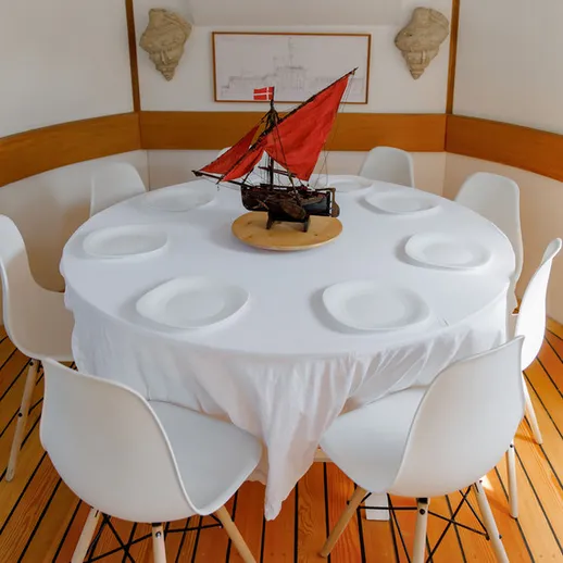 Круглый стол с белой скатертью и моделью корабля в морском интерьере