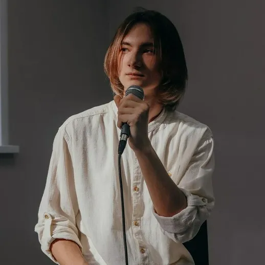 Молодой человек с микрофоном делится мыслями о жизни в уютной обстановке в начале вечера во время беседы