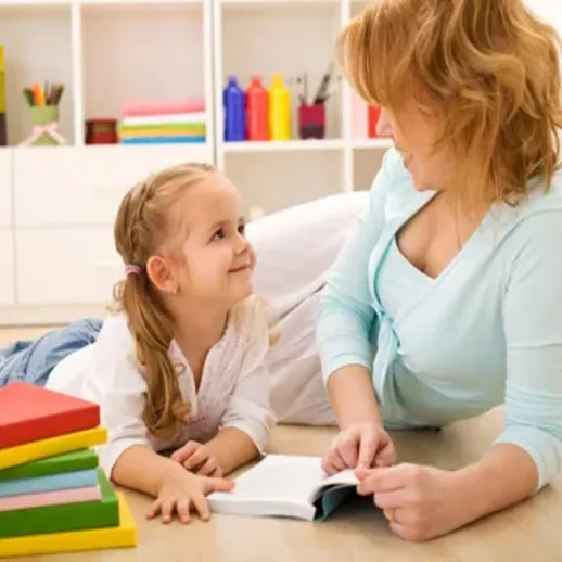 Мама и дочь читают книгу на полу в уютной детской комнате с яркими игрушками и книгами