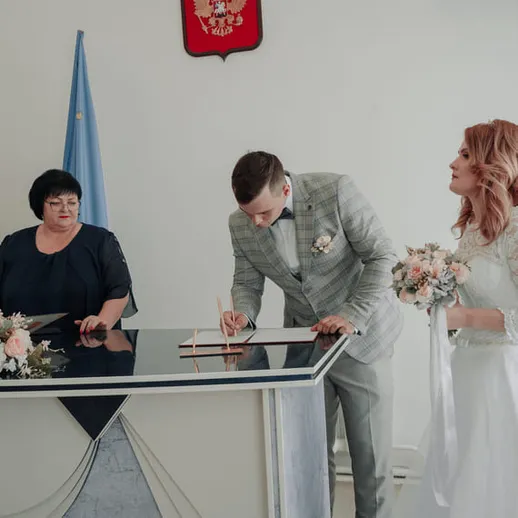 Церемония регистрации брака в загсе, молодожёны подписывают документы и обмениваются взглядами
