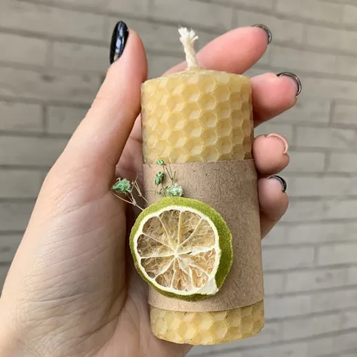 Свеча из воска с лимоном и зеленью в руке на фоне стены