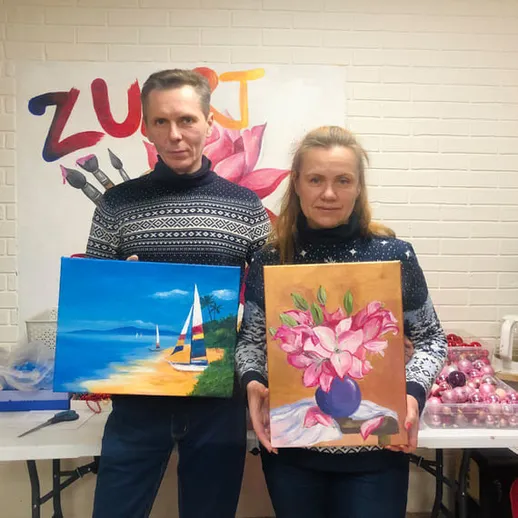 Участники художественного мастер-класса показывают свои картины на фоне творческой атмосферы