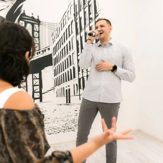 Мужчина поет в помещении с настенной росписью и слушает женщина